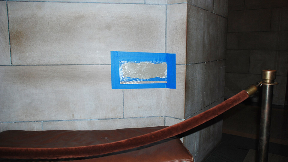 Poultice application: A mason tests a spot to remove body oil from the wall behind an elevator bench.