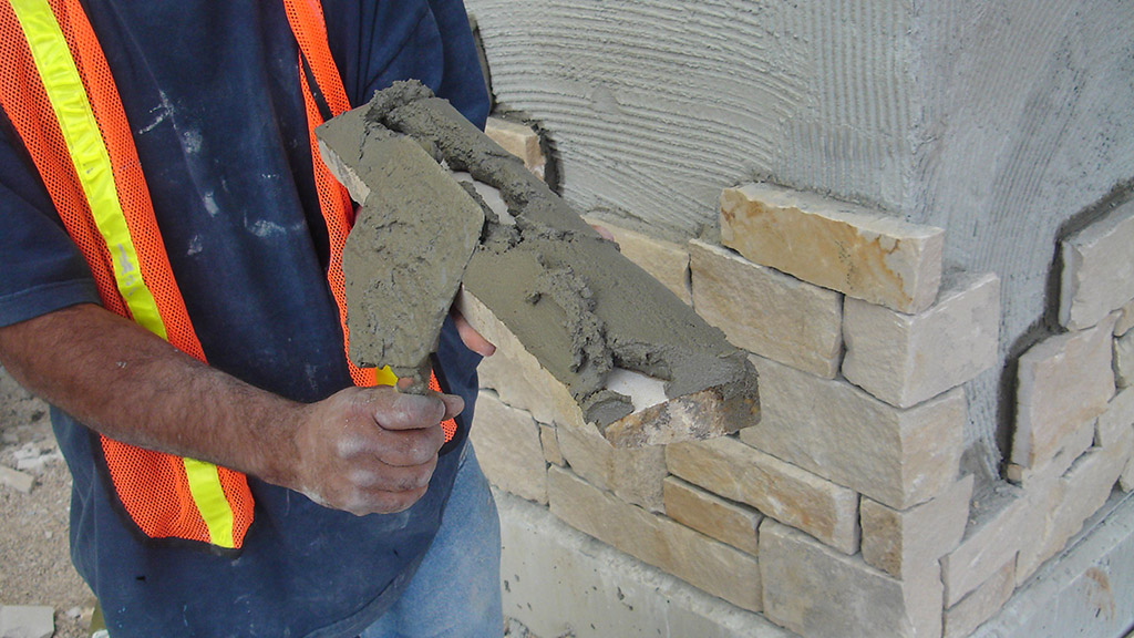 Mortar is being applied to an adhered masonry unit before placement.