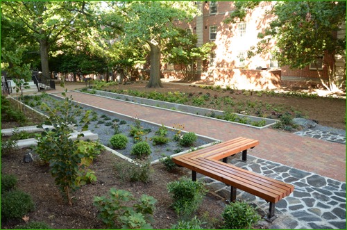 So it stands to reason that teaching green construction techniques to today’s students also bodes well for the future of construction. That future will center on using sustainable materials within projects with a role to play in protecting the planet. The Artist’s Backyard is a joint project between N.C. State University’s departments of Landscape Architecture and University Housing. It’s a plaza and rain garden between two older dormitories, Owen and Turlington Halls. It uses a combination of StormPave permeable pavers from Pine Hall Brick, along with materials that were recycled from a building demolition. New benches anchor a gathering spot where students visit with each other, read a book or text their friends.  Andrew Fox, an assistant professor at the NCSU College of Design, says The Artists Backyard is an outgrowth of last year’s renovation of Syme Hall on East Campus. Fox pursued a $20,000 teaching grant through the university to lead his students through a design-build exercise to improve the Syme Hall site from a muddy mess to a beautiful rain garden. The success of that project prompted Dr. Tim Luckadoo, associate vice chancellor for student affairs, who oversees housing on campus, to talk with Fox about additional projects. Those discussions turned into $175,000 in funding and a five-year plan to improve the landscapes around several N.C. State residence halls. It’s a win for both sides. Students get the real-world experience of designing and helping construct natural common areas, and the university gets cost-effective improvements to its surroundings. Before The Artist’s Backyard was built, surging stormwater would carry leaves and other debris across the existing concrete sidewalk. The solution is to use Low Impact Development design techniques to slow, capture and clean stormwater on site. Cisterns and the permeable paver installation re-direct stormwater into the rain garden and the ground, effectively filtering it and preventing erosion. Nine days after the installation was complete, Mother Nature handed the college students a pop quiz. Thunderstorms rolled across central North Carolina and dropped 4.69 inches of rain, amounting to a 100-year flood. “The surface water drained into the rain garden and it was dry, no puddling,” says Fox. “The rain garden had handled that huge pulse of rain water. After four hours, the test wells were slowly infiltrating and the water was not standing.”