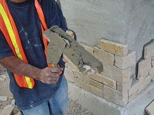 Mortar is being applied to an adhered masonry unit before placement.